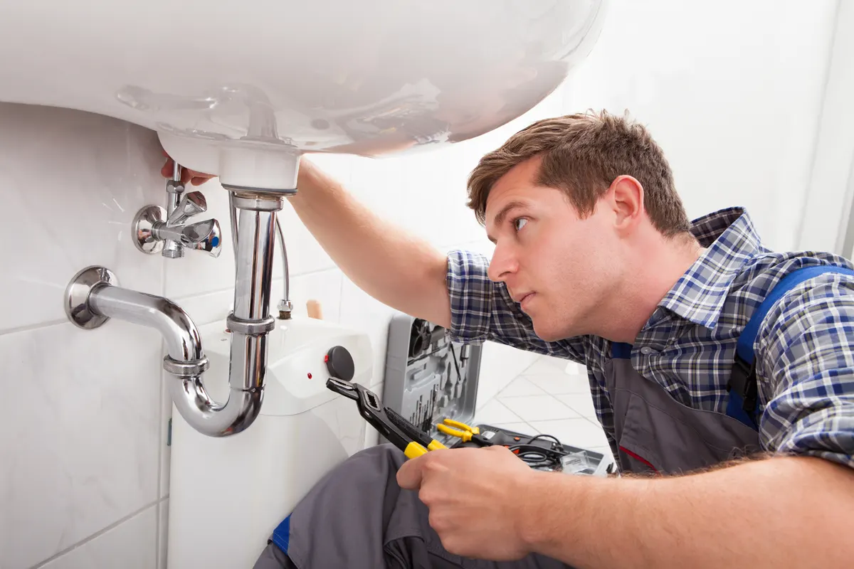 A plumber fixing a sink pipe with the help of technology provided by Managed Services Australia