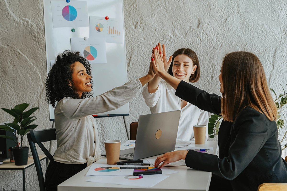 Embracing Diversity and Inclusion – Team Celebration Group_high_fiving_at_table_with_laptop_Managed_Services_Australia